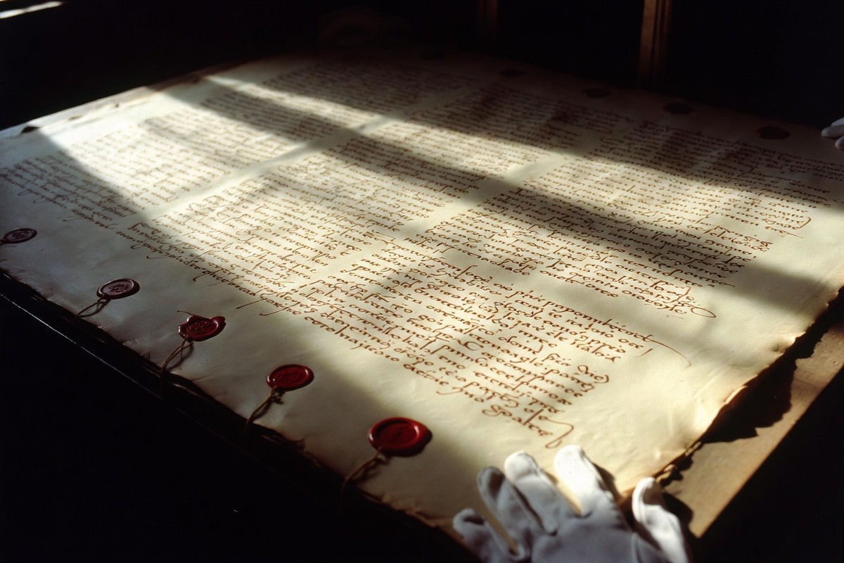 Das Pergament von Chinon aus dem Jahr 1308 ausgebreitet auf einem Archivtisch, mit anhängenden roten Wachssiegeln und den behandschuhten Händen eines Archivars